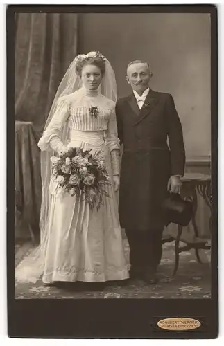 Fotografie Adalbert Werner, München, älteres Ehepaar im Hochzeitskleid und Anzug mit Brautstrauss und Zylinder