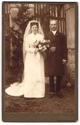 Fotografie Carl John, Ehrenhain i. Sa., sächsisches Brautpaar im Hochzeitskleid und Anzug vor dem Wohnhaus