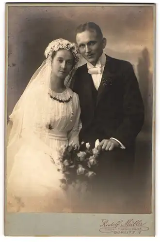 Fotografie Rudolf Müller, Görlitz, junges Ehepaar mit Brautstrauss im Hochzeitskleid und Anzug