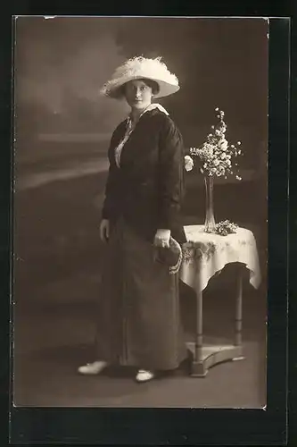 Foto-AK Frau in Ausgehgarderobe mit Hut vor einem Blumengedeckten Tisch