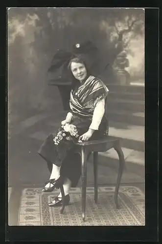 Foto-AK Kind mit übergrosser Schleife auf dem Kof und Blumen in der Hand auf einem Stuhl