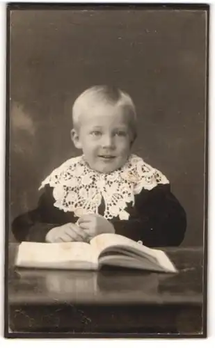 Fotografie Atelier Blomgren, Klippan, Portrait hübsch gekleidetes Kind mit Buch am Tisch