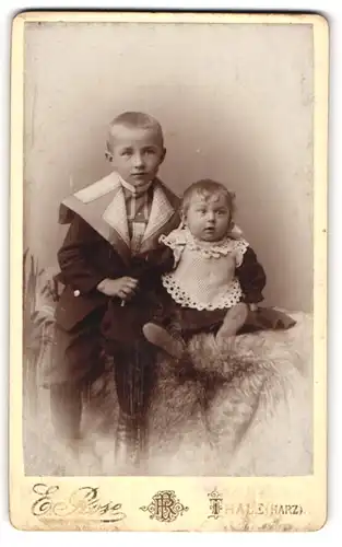 Fotografie E. Rose, Thale / Harz, Geschwister in Sonntagskleidung sitzend auf einem Fell