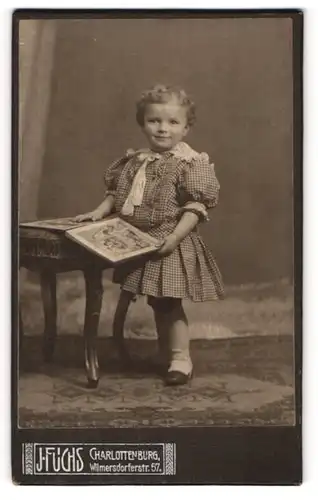 Fotografie J. Fuchs, Charlottenburg, Kleinkind im karrierten Kleid mit Buch