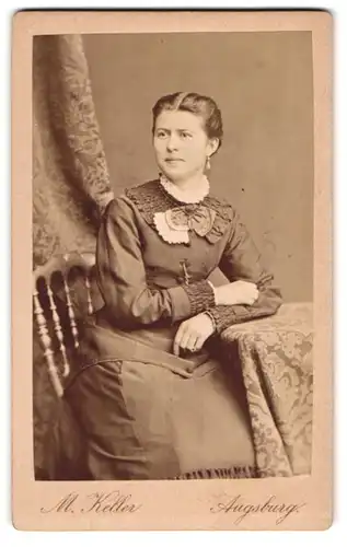Fotografie M. Keller, Augsburg, Portrait hübsch gekleidete Dame am Tisch sitzend
