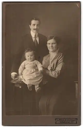 Fotografie L. Möhle, Stuttgart, Portrait bürgerliches Paar mit Kleinkind am Tisch