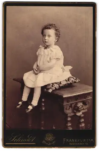 Fotografie J. Schmidt, Frankfurt a / M., Portrait kleines Mädchen im weissen Kleid auf Kissen sitzend