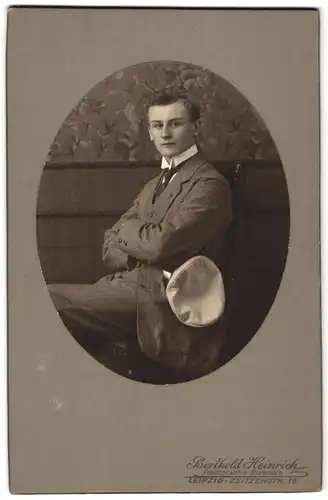 Fotografie Berthold Heinrich, Leipzig, Portrait sitzender Herr im Anzug mit verschränkten Armen und Schirmmütze