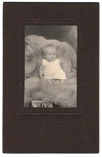 Fotografie Alwin Trautmann, Grossröhrsdorf, Portrait niedliches Baby im weissen Hemd auf Fell sitzend