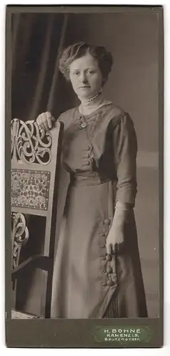 Fotografie H. Bohne, Kamenz i. S., Portrait modisch gekleidete Dame mit Medaillon an Stuhl gelehnt