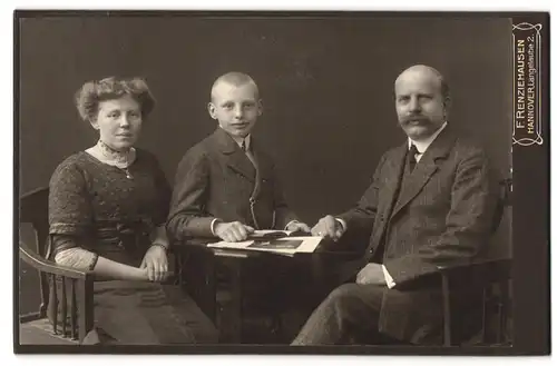 Fotografie F. Renziehausen, Hannover, Portrait bürgerliches Paar und Junge mit Buch am Tisch