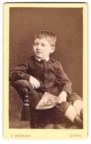 Fotografie G. Brokesch, Leipzig, Portrait hübsch gekleideter Junge mit Heft auf Sessel sitzend