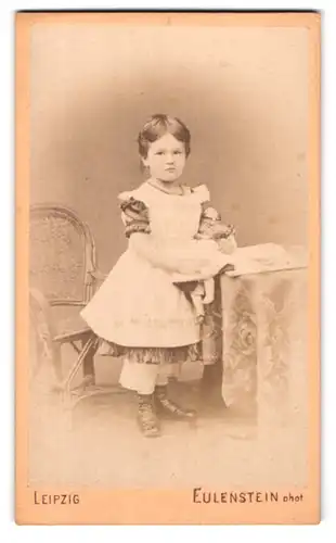 Fotografie Eulenstein, Leipzig, Portrait kleines Mädchen mit Puppe und Buch am Tisch