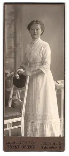 Fotografie Erst Oehme, Freiberg, Portrait weiss gekleidete Dame mit Blumen an Stuhl gelehnt