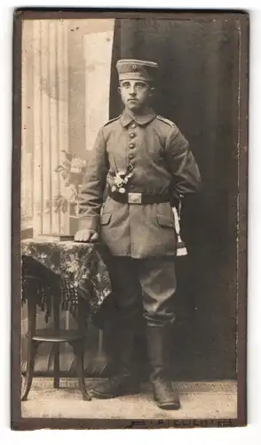 Fotografie unbekannter Fotograf und Ort, Portrait Soldat in Uniform an Tisch gelehnt