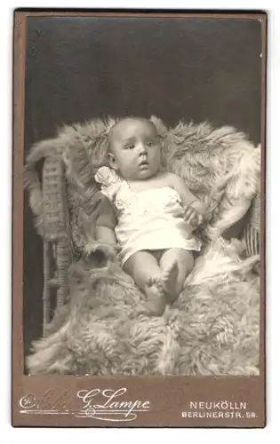 Fotografie Georg Lampe, Berlin-Neukölln, Portrait niedliches Kleinkind im weissen Hemd auf Fell liegend