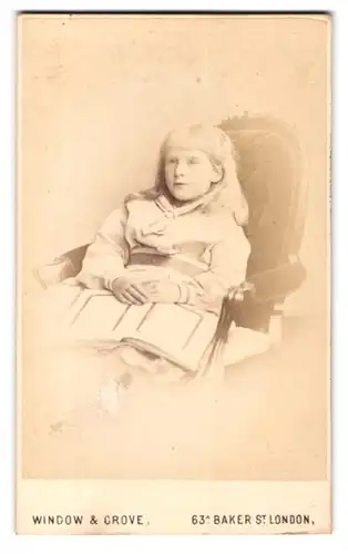 Fotografie Window & Grove, London-W, Portrait hübsch gekleidetes Mädchen mit Buch auf Stuhl sitzend