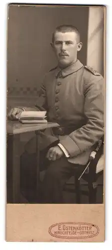 Fotografie E. Ostenkötter, Hirschfelde-Ostritz, Portrait Soldat in Uniform mit Buch am Tisch sitzend