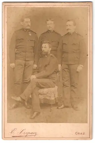 Fotografie E. Czepan, Graz, Portrait vier Soldaten in Uniform am Stuhl