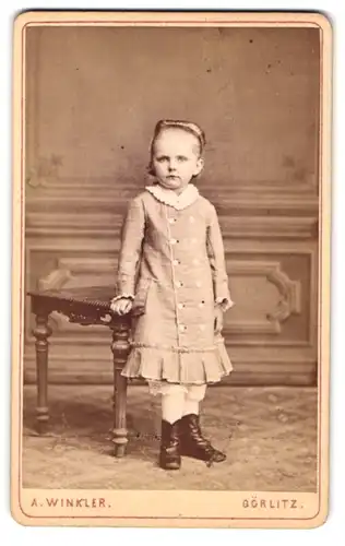 Fotografie A. Winkler, Görlitz, Portrait hübsch gekleidetes Mädchen an Tisch gelehnt