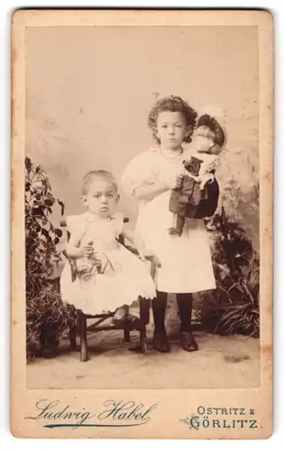 Fotografie Ludwig Habel, Görlitz, zwei niedliche kleine Mädchen mit Blechfigur auf Dreirad / Fahrrad und Puppe im Arm