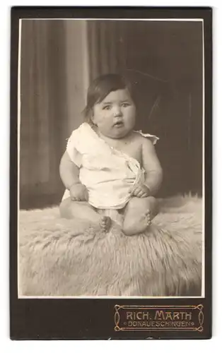 Fotografie Rich. Marth, Donaueschingen, Portrait niedliches Kleinkind im weissen Hemd auf Fell sitzend