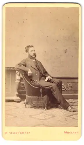 Fotografie M. Pössenbacher, München, Portrait eleganter Herr mit Bart und Buch auf Sessel sitzend