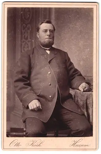 Fotografie Otto Koch, Husum, Portrait modisch gekleideter Herr mit Bart am Tisch sitzend