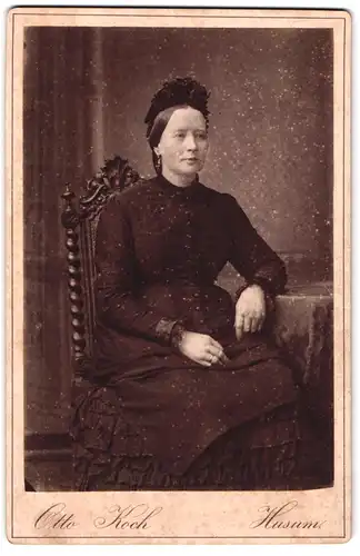 Fotografie Otto Koch, Husum, Portrait schwarz gekleidete Dame mit Haube am Tisch sitzend