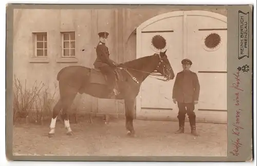 Fotografie Reinh. Bertuch, Prenzlau, Ansicht Prenzlau /Ucker, Soldat mit Pferd vor einem Stall, Inf. Rgt Nr. 64
