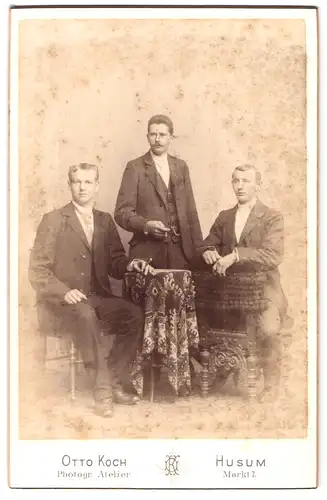 Fotografie Otto Koch, Husum, Markt 7, Portrait drei elegant gekleidete Herren mit Zigarren am Tisch