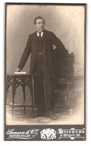 Fotografie Samson & Co, Duisburg, Königstrasse 38, Mann im Anzug mit Taschenuhr stehend am Tisch