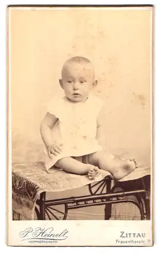 Fotografie P. Heinelt, Zittau, Frauenthorstr. 7, Verdutzter Säugling sitzt auf Tisch