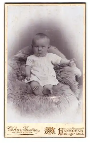 Fotografie Oskar Goetze, Hannover, Heiliger Str. 3, Portrait niedliches Kleinkind im weissen Hemd auf Fell sitzend