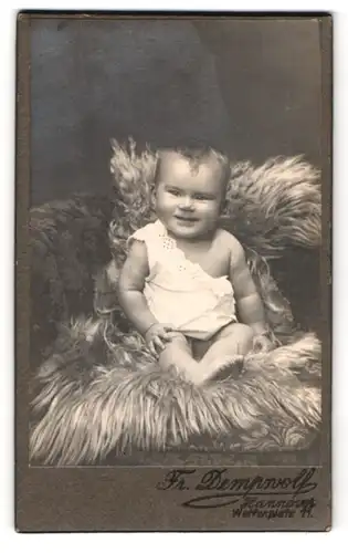 Fotografie Fr. Dempwolf, Hannover, Welfenplatz 11, Portrait niedliches Baby im weissen Hemd auf Fell sitzend