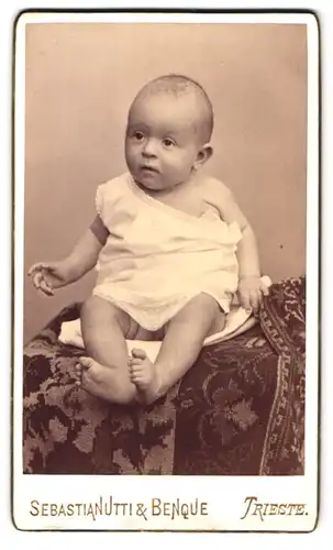 Fotografie Sebastianutti & Benque, Trieste, Portrait niedliches Baby im weissen Hemd auf Decke sitzend