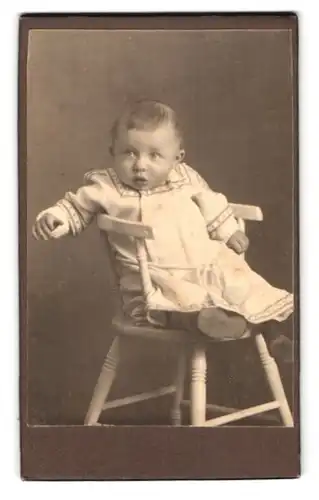 Fotografie unbekannter Fotograf und Ort, Portrait niedliches Baby im hübschen Kleid auf Stuhl sitzend