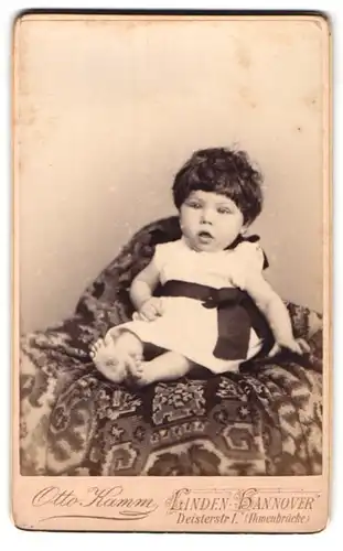 Fotografie Otto Kamm, Hannover-Linden, Deisterstrasse 1, Portrait niedliches Kleinkind im weissen Kleid auf Decke sitzend