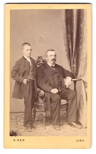 Fotografie August Red, Linz, Portrait bürgerlicher Herr auf Stuhl sitzend mit einem Jungen