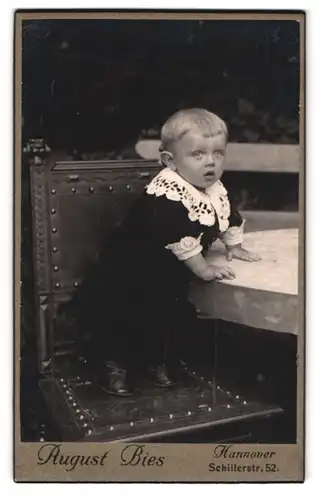 Fotografie August Bies, Hannover, Schillerstrasse 52, Portrait süsses Kleinkind in hübscher Kleidung auf Stuhl stehend