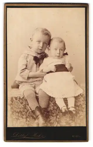 Fotografie Detlef Hann, Kiel, Brunswieckerstrasse 14, Portrait Kinderpaar in hübscher Kleidung auf Tisch sitzend