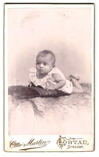 Fotografie Otto Martin, Löbtau, Dresden, Portrait niedliches Baby im weissen Hemd bäuchlings auf Fell liegend