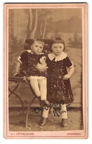 Fotografie A.J. Köppelmann, Arnsberg, Chausseestrassre 136, zwei Mädchen in Sonntagskleidern an einem Stuhl