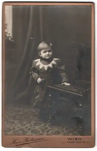 Fotografie Heinr. Hartmann, Wien, Wiedner-Hauptstr. 97, Kleinkind in festlicher Kleidung stützt sich an Stuhl auf