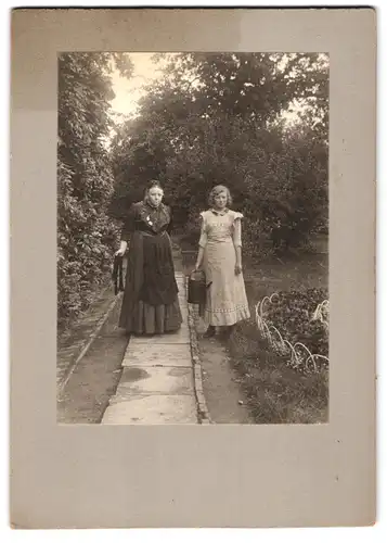 Fotografie Fotograf und Ort unbekannt, Ältere und jüngere Frau in Trachten auf einem Gartenweg mit Giesskanne in der Hand