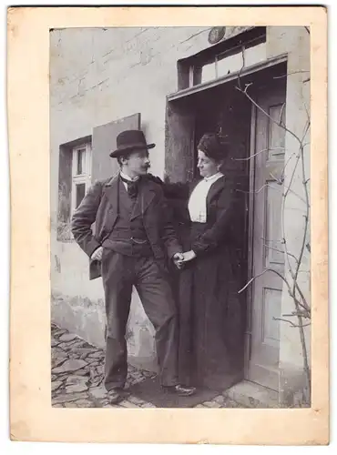 Fotografie Portrait Frau im dunklen Kleid verabschiedet Mann im Anzug mit Hut an der Haustür