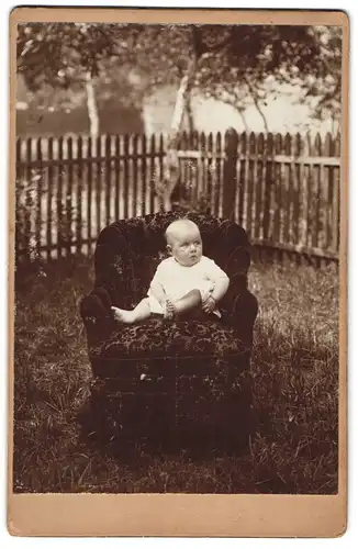 Fotografie unbekannter Fotograf und Ort, Portrait niedliches Baby im weissen Hemd auf Sessel sitzend