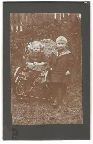 Fotografie unbekannter Fotograf und Ort, Geschwisterpaar, Mädchen sitzt auf einem Stuhl