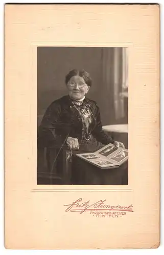 Fotografie Fritz Jungcurt, Rinteln, Greise Frau in elegantem Kleid blättert in einem Fotoalbum