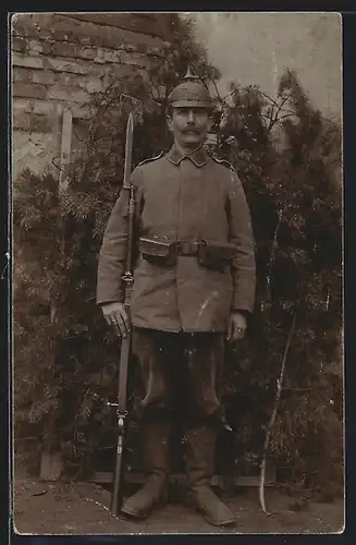 Foto-AK Soldat in Feldgrau Uniform mit preussischer Ersatz Pickelhaube, Ersatz-Bajonett auf Gewehr